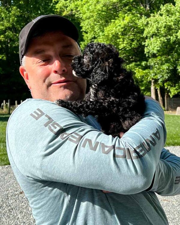 Man holding a black Cavapoo puppy in his arms