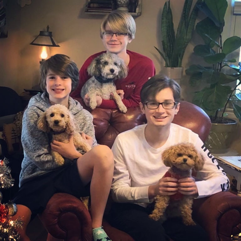 Three young boys sitting on a couch each holding a puppy