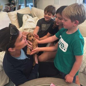 Adult woman holding a puppy Cavapoo and showing it to litlle kids