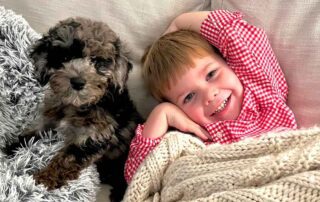 Litlle girl laying in bed with a puppy Cavapoo and smiling