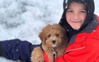 Cream Cavapoo puppy laying on a boy's laps in the snow