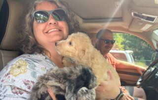 woman holding two male Cavapoo puppies in a car