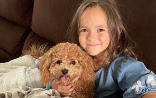 Young girl sitting down on a couch with a puppy Cavapoo on her laps