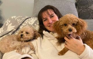 Two Cavapoos laying down in a couch with a woman in the middle