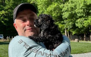 Man holding a black Cavapoo in his arms