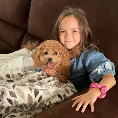 Young girl sitting down in a couch with a puppy with a blanket over them